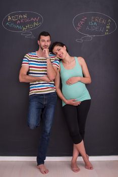 young pregnant couple thinking about names for their unborn baby and writing them on a black chalkboard