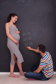 young pregnant couple accounts week of pregnancy and writing them with chalk on blackboard