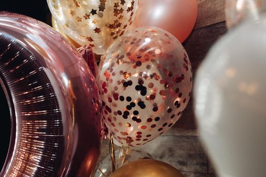 Stock photo of bright festive air balloons with sparkling elements inside inflated with helium at party.