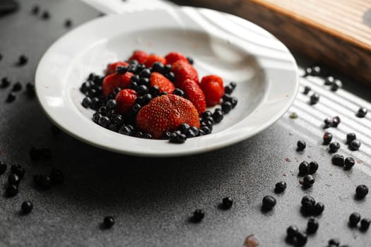 Top view of strawberries and black currants in a white plate near the window. Healthy food concept