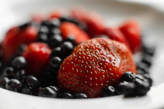 Top view of berries fresh colorful assortment, strawberries and black currants on white plate. Healthy food concept