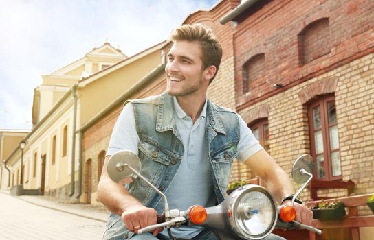 Cheerful young man is riding on scooter in town.