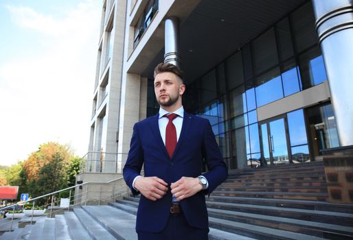 Portrait of a handsome businessman in a suit standing outside a city building.