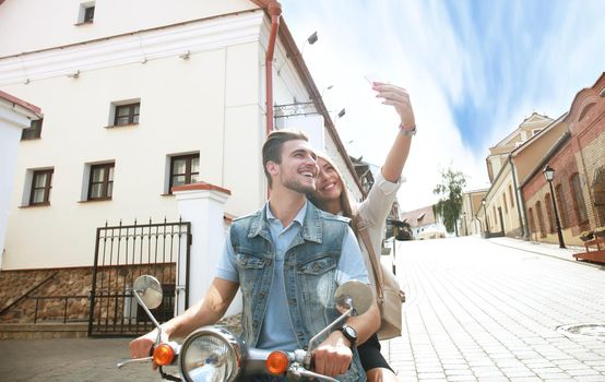 Happy couple on scooter making selfie photo on smartphone outdoors