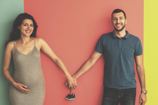 young pregnant couple holding newborn baby shoes isolated on colorful background,family and parenthood concept