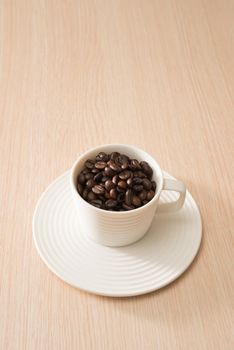 Cup of full coffee beans on the wood background