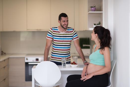 young pregnant couple eating strawberries at kitchen, lifestyle healthy pregnancy happy life concept