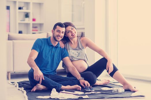 a happy pregnant couple checking a list of things for their unborn baby at home on the floor