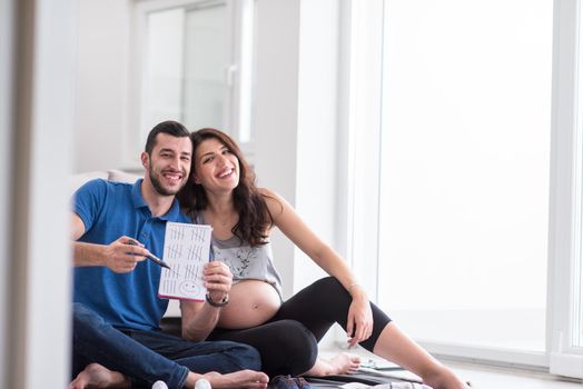 a happy pregnant couple checking a list of things for their unborn baby at home on the floor