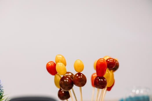 Assorted red and yellow cherry tomatoes on wooden sticks on white background. Copy space. Snack and food concept.