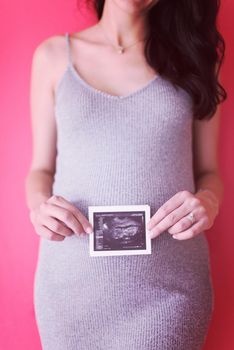 smiling pregnant woman showing ultrasound picture of her unborn baby isolated on red background