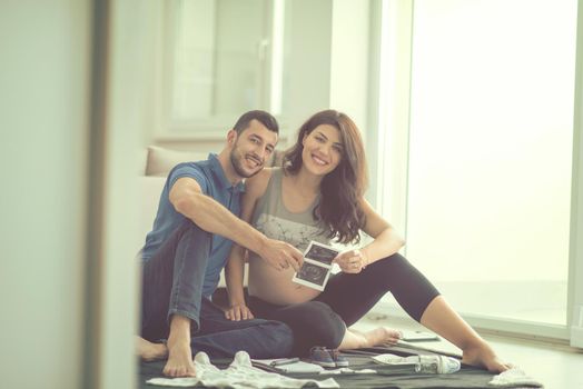 a happy pregnant couple checking a list of things for their unborn baby at home on the floor