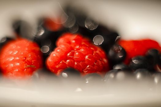 Macro stock photo of fresh, sweet and organic black currant on red ripe raspberries.