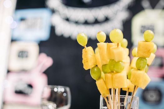 Tasty canapes with cheese and green grapes in glass at party on blurred background. Party snacks and food concept.