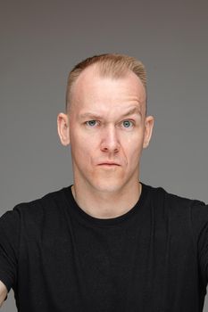 adult caucasian man in black t-shirt and short fair hair looks to the camera with a doubt