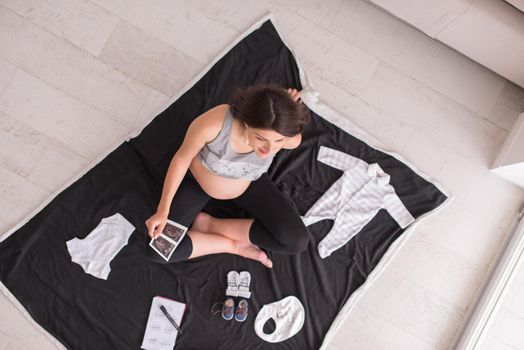 a pregnant woman at home on the floor checking list of baby clothes preparing for going to maternity hospital top view.Pregnancy, birth concept