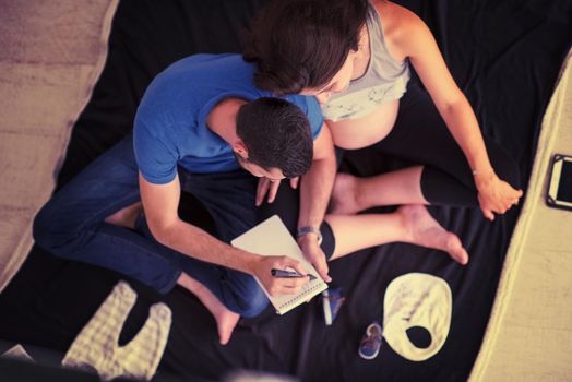 top view of a happy pregnant couple checking a list of things for their unborn baby at home on the floor