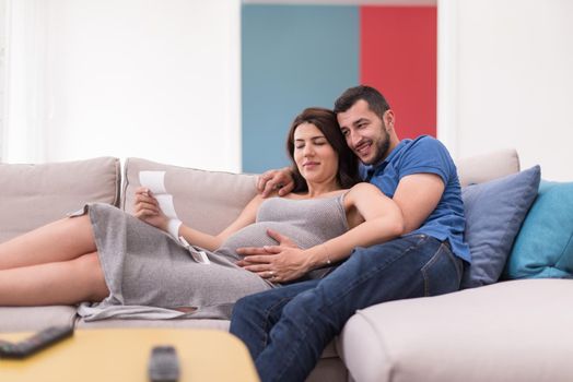 Young pregnant couple looking baby's ultrasound photo while relaxing on sofa at home