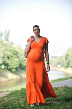 beautiful young happy pregnant woman outdoor in bright nature in orange dress