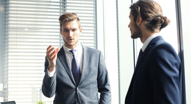 Mature businessman using a digital tablet to discuss information with a younger colleague in a modern business office.