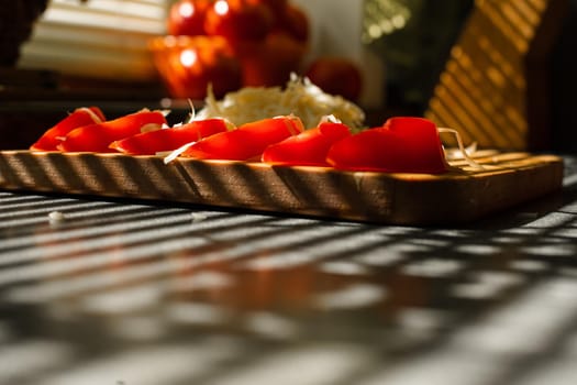 Stock photo in close up of sliced tomatoes with shredded cheese on wooden board in sunlight. Blinds shadow over the table. Cooking process.