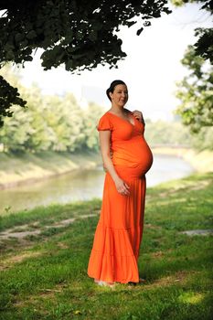 beautiful young happy pregnant woman outdoor in bright nature in orange dress