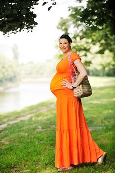 beautiful young happy pregnant woman outdoor in bright nature in orange dress