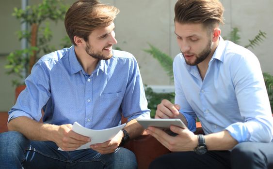 Mature businessman using a digital tablet to discuss information with a younger colleague in a modern business office