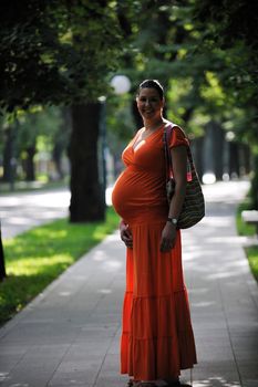 beautiful young happy pregnant woman outdoor in bright nature in orange dress