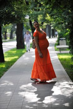 beautiful young happy pregnant woman outdoor in bright nature in orange dress