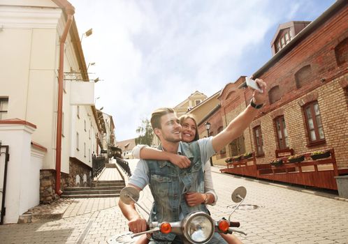 Happy couple on scooter making selfie photo on smartphone outdoors