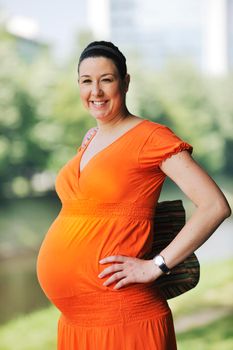 beautiful young happy pregnant woman outdoor in bright nature in orange dress