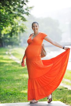 beautiful young happy pregnant woman outdoor in bright nature in orange dress