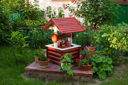 Landscape of a small decorative well with a lot of color near it in the big garden in summer