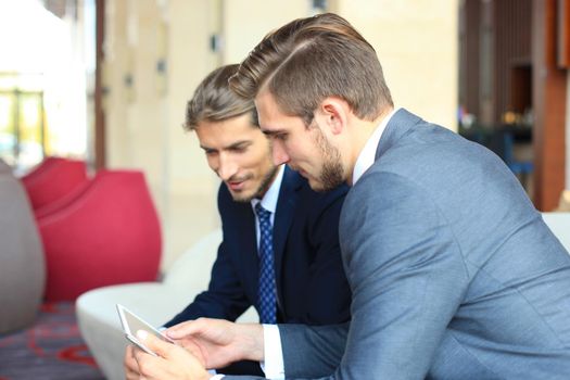 Two young businessmen using touchpad at meeting.