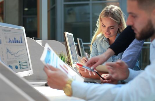 Group of young people in casual wear sitting at the office desk and discussing something while looking at PC together.