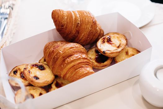 Bakery products, baked sweet croissants, cakes in packaging cardboard box on table for breakfast. Hotel catering. High quality photo