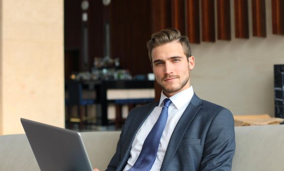 Young businessman working on laptop, sitting in hotel lobby waiting for someone