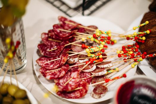 Close-up of delicious sausage snacks on sticks at party on served table. Variety of sausages slices on sticks with colorful decorations.