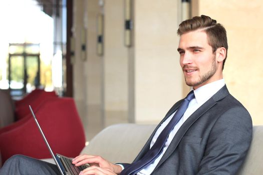 Young businessman working on laptop, sitting in hotel lobby waiting for someone