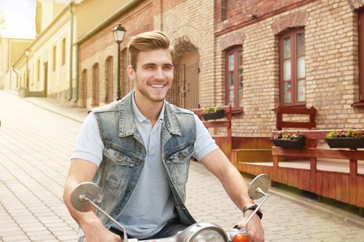 Cheerful young man is riding on scooter in town.