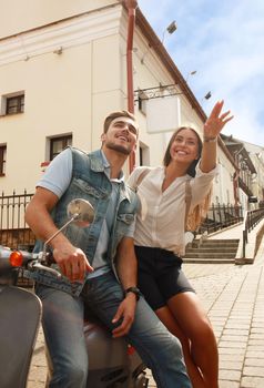 happy young couple riding scooter in town. Handsome guy and young woman travel. Adventure and vacations concept.