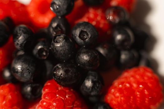 Macro stock photo of fresh, sweet and organic black currant on red ripe raspberries.