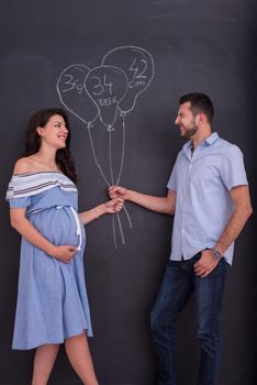 Conceptual photo of pregnant couple drawing their imaginations about the future life with children on chalk board