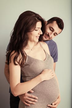 Portrait of a happy young couple,man holding his pregnant wife belly isolated over blue background