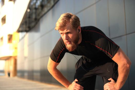 Handsome young man after run resting after jog in the city at sunset or sunrise