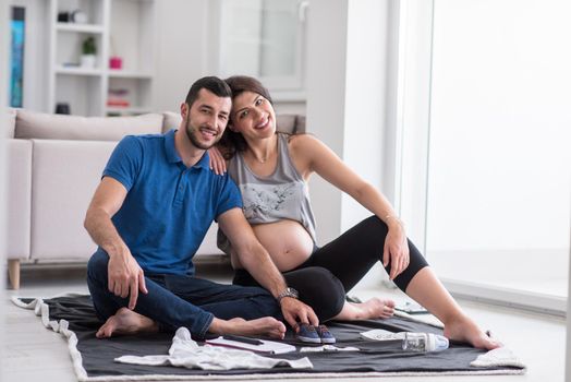 a happy pregnant couple checking a list of things for their unborn baby at home on the floor