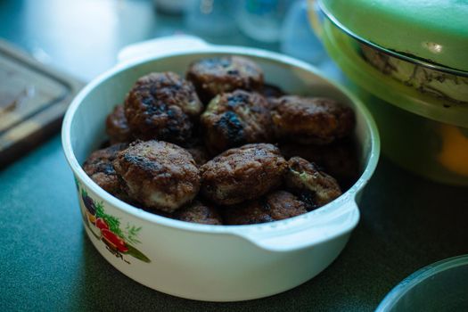 Plenty of ready-made fried meatballs lie in a large white aluminum pan on the table.