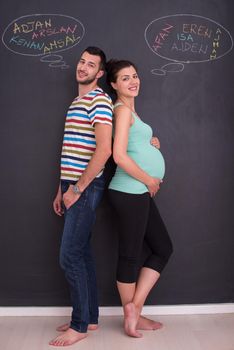 young pregnant couple thinking about names for their unborn baby and writing them on a black chalkboard