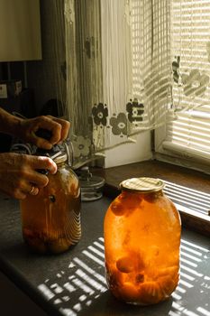 A woman rolls a compote in a large jar under the sun in summer at home in the village.